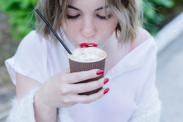 Girl with red lips takes a sip of cappuccino from paper cup