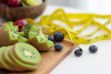Closed up on fresh green kiwi, blueberries, strawberries and measurement tape on white background. Healthy and dietary concept.