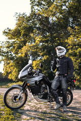 rider guy use smart phone in jeans biker jacket and helmet sit on tourist touring motorcycle. outdoors, dual sport adventure concept, vertical photo, dirt road