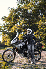 rider guy use smart phone in jeans biker jacket and helmet sit on tourist touring motorcycle. outdoors, dual sport adventure concept, vertical photo, dirt road