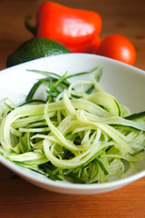 Raw cucumber green spaghetti in white bowl with vegetables at wooden table vertical