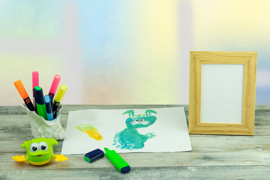 Happy childrens day. Workplace from child is painting his mother a bunny picture and a empty wooden frame over bright pastel background. Space for your design.
