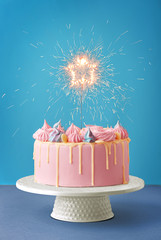 Birthday cake isolated on a blue background. Birthday party decorated cake with candles and sparkles. Copy space