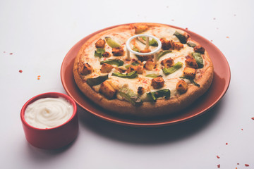 Paneer Pizza is an indian version of Italian dish topped with Cottage Cheese, served in a plate with white sauce. selective focus
