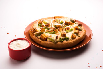 Paneer Pizza is an indian version of Italian dish topped with Cottage Cheese, served in a plate with white sauce. selective focus
