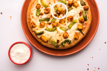 Paneer Pizza is an indian version of Italian dish topped with Cottage Cheese, served in a plate with white sauce. selective focus