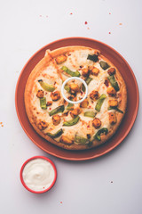 Paneer Pizza is an indian version of Italian dish topped with Cottage Cheese, served in a plate with white sauce. selective focus