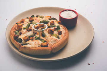 Paneer Pizza is an indian version of Italian dish topped with Cottage Cheese, served in a plate with white sauce. selective focus