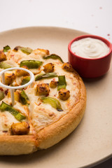 Paneer Pizza is an indian version of Italian dish topped with Cottage Cheese, served in a plate with white sauce. selective focus