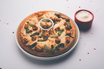 Paneer Pizza is an indian version of Italian dish topped with Cottage Cheese, served in a plate with white sauce. selective focus