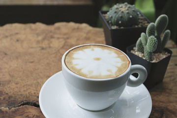 A cup of latte art on wood table in morning, Coffee with a pattern of milk in white cup. A cup of coffee with small cute cactus.
