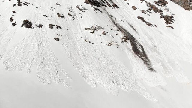 Aerial: flying close to snow avalanche on mountain snowy slope reveals in springtime