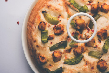 Paneer Pizza is an indian version of Italian dish topped with Cottage Cheese, served in a plate with white sauce. selective focus