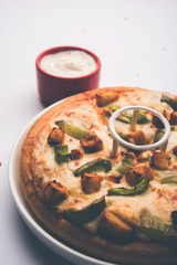 Paneer Pizza is an indian version of Italian dish topped with Cottage Cheese, served in a plate with white sauce. selective focus