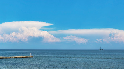 Naklejka premium Blue sea under clouds sky with the ship on the horizon and fisherman on the pier