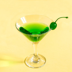Green cocktail with maraschino cherry in martini glass
