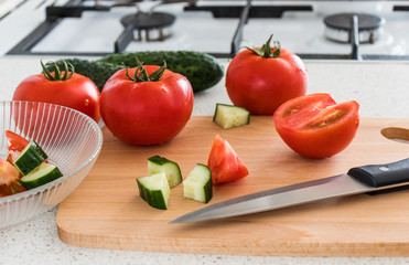 Making salad in the kitchen. Tomato and cucumber, wooden board and knife