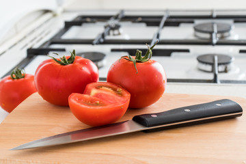  Tomato and knife on wooden board in the kitchen.