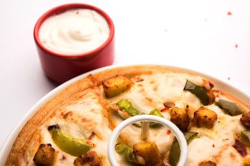 Paneer Pizza is an indian version of Italian dish topped with Cottage Cheese, served in a plate with white sauce. selective focus