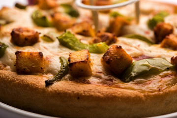 Paneer Pizza is an indian version of Italian dish topped with Cottage Cheese, served in a plate with white sauce. selective focus