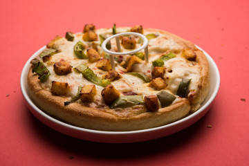 Paneer Pizza is an indian version of Italian dish topped with Cottage Cheese, served in a plate with white sauce. selective focus