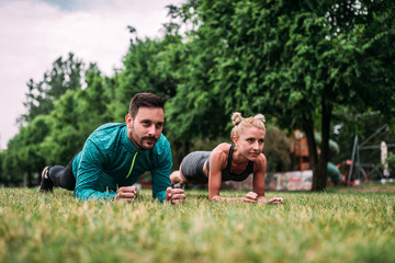 Couple doing plank exercise outdoors.