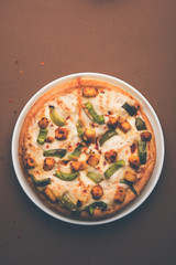 Paneer Pizza is an indian version of Italian dish topped with Cottage Cheese, served in a plate with white sauce. selective focus