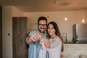 Young happy couple showing keys of new home. Looking at camera.