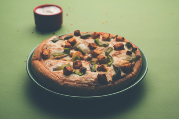 Paneer Pizza is an indian version of Italian dish topped with Cottage Cheese, served in a plate with white sauce. selective focus