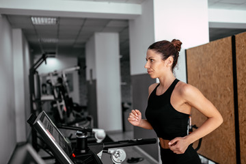 Side view of attractive sports woman running on treadmill.