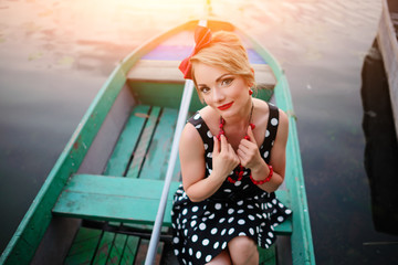 Beautiful young woman dressed dressed in a boat on a lake shore