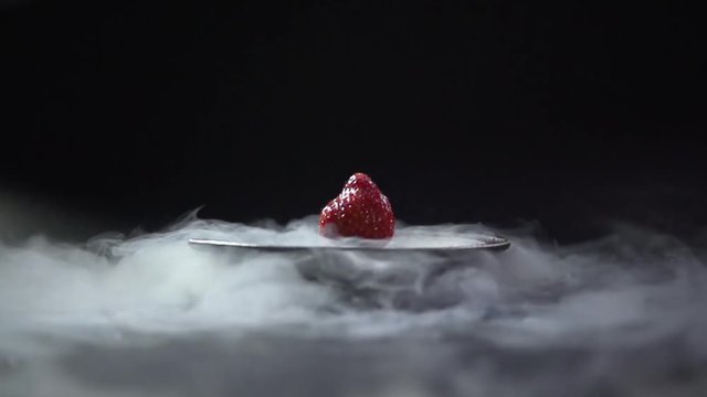 Strawberries lie in the middle of the plate from which the smoke is poured.