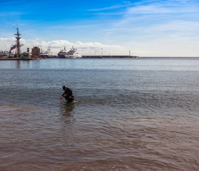 A man in a diving suit is looking for coins with a metal detector at the bottom of the bay