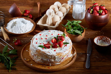 Strawberry tart covered with whipped sour cream surrounded by organic ingredients over wooden background, flat lay.