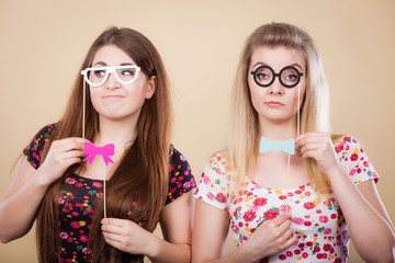 Two serious women holding carnival accessoies on stick