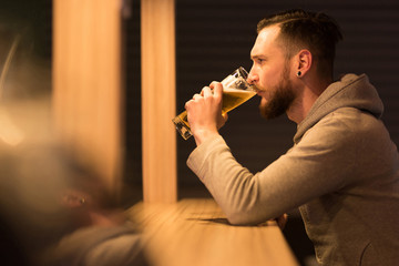 A handsome young hipster man drinking a beer at the bar.