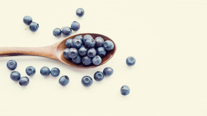 Fresh blueberries in a wooden spoon on a light  surface of a table. Closeup, top view.