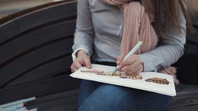 close up shot of the artist's hands, who draws the markers on the paper for the sketches, the lady paints the sketch with different markers