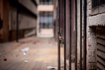 A metal barred doorway with a padlock standing open against the background of a dirty alley way in Johannesburg inner city