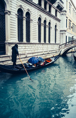Tourists in a gondola with umbrella under heavy rain in a small canal. Venice, Italy