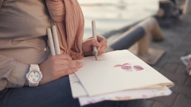 close up shot of the artist's hands, the lady holds the markers and draws on the paper for the sketches the abstract drawing, the woman is on the planner