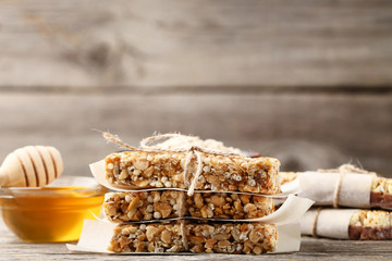 Tasty granola bars with honey in bowl on wooden table