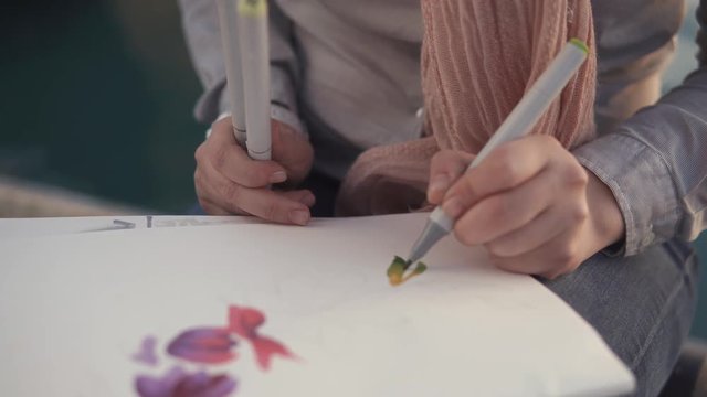 Close up shot of a young and talented artist carefully coloring her drawing outdoor. Woman working on her pictures on the streets.