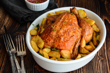Chicken baked with potatoes in a white bowl.