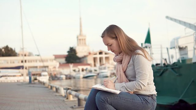 a young woman is on a planner near the river, perhaps this is a port, a woman is engaged in painting and sells her pictures to a street fair