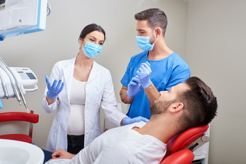 A handsome dentist and a young assistant consulting with the patient in the dentists chair.