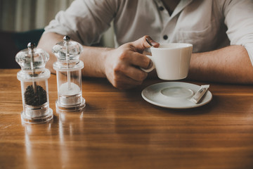 closeup of man's hands hold a cup of coffee on a wooden table with salt and pepper