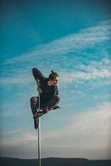 Athletic man makes beautiful athletic, acrobatic elements on a portable pylon on the blue sky background