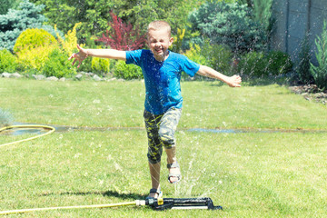 Fototapeta premium Boy running on the lawn sprinkler playing with water splashes . Summer vacation day.