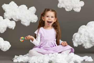 girl girl eating candy and playing with clouds, shooting in the studio on a gray background, happy childhood concept